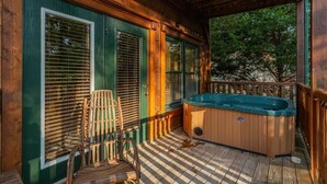 A wooden deck with a hot tub, a chair, and a window with blinds.