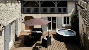 Um deck de madeira com mobiliário externo, uma banheira de hidromassagem e um muro de pedra.