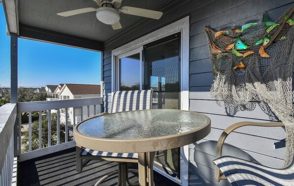 Un espace extérieur abrité, avec une table et des chaises en verre, un ventilateur de plafond et une sculpture décorative représentant un poisson.