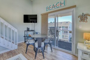 A room with a dining table and chairs, a TV mounted on the wall, and a balcony with a view of buildings.