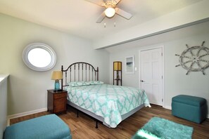 Un dormitorio con cama, ventanal redondo, ventilador de techo, timón de barco y puerta.