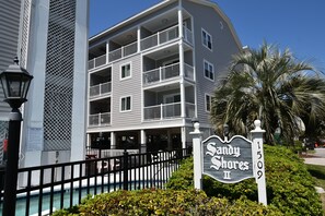 Un hôtel à plusieurs étages doté de balcons, d’un espace piscine et d’une enseigne indiquant « Sandy Shores II ».