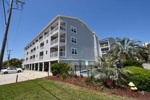 Um edifício com várias andares, varandas, piscina e área de estacionamento.