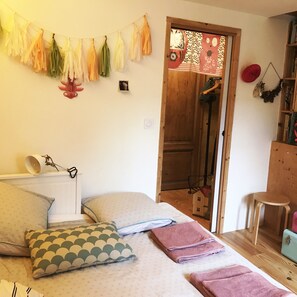 A cozy bedroom with a bed, pillows, a hanging light, a wooden door, and a small table.
