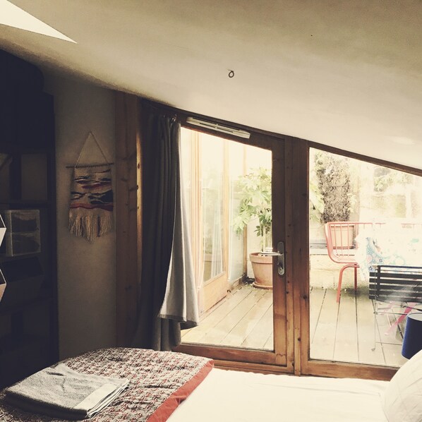 A bedroom with a large bed, a sliding glass door leading to an outdoor patio with a chair and a table.