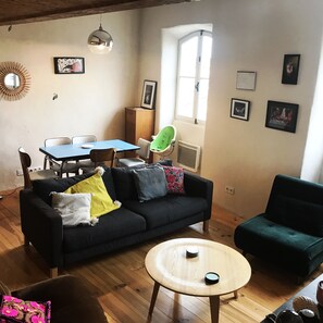 A cozy living room with a black sofa, a round wooden coffee table, a green armchair, and a dining area with a blue table and chairs.