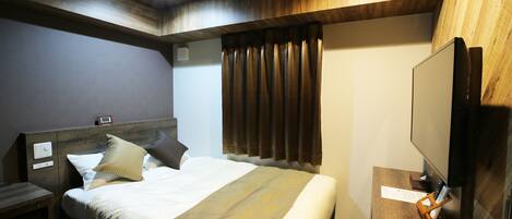 A hotel room with a wooden ceiling, a bed with a beige bedspread and pillows, a nightstand, a TV on a wooden stand, and a window with curtains.