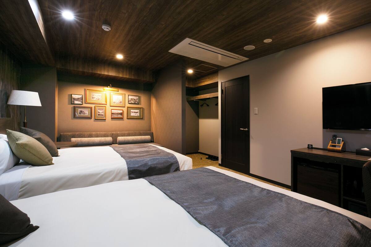 Ein Hotelzimmer mit zwei Betten, einem Fernseher, einem Kleiderständer und gerahmten Bildern an der Wand.