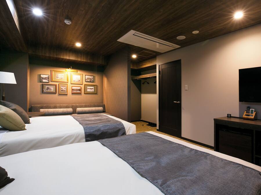 Ein Hotelzimmer mit zwei Betten, einem Fernseher, einem Kleiderständer und gerahmten Bildern an der Wand.