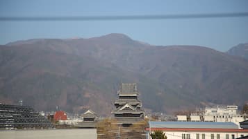 Un bâtiment japonais traditionnel, doté d’un toit à plusieurs niveaux, entouré de bâtiments modernes et avec des montagnes en arrière-plan.