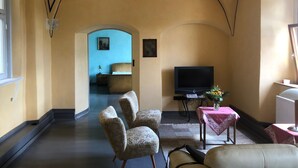 Een woonkamer met een bank, fauteuils, een televisie en een tafel met een vaas.