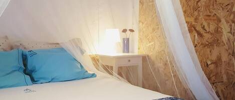 A bed with a blue and white patterned bedspread, a white bedside table with a lamp, and a blue pillow.