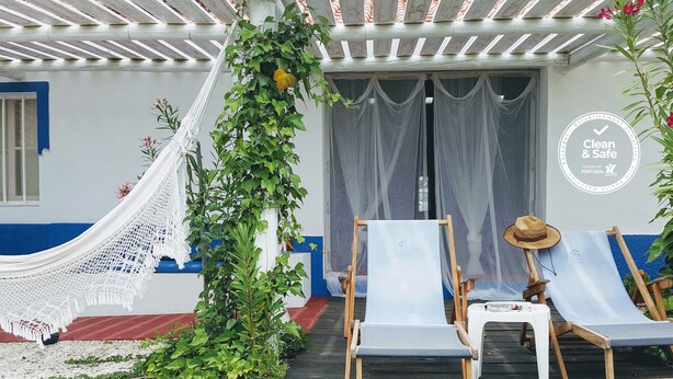 A covered outdoor seating area with two lounge chairs, a hammock, and a sign indicating 'Clean & Safe' and 'Portugal'.