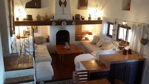 Un espacio habitable acogedor y funcional con cama tipo altillo, sofá, mesa de comedor y zona de cocina con estantes superiores.