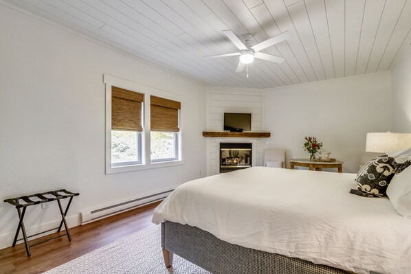 A bedroom with a large bed, a ceiling fan, a fireplace, a TV, and a small table with a vase. - Historic Farm, Near Lake, 10 Acres, Newly Renovated (Swanton)