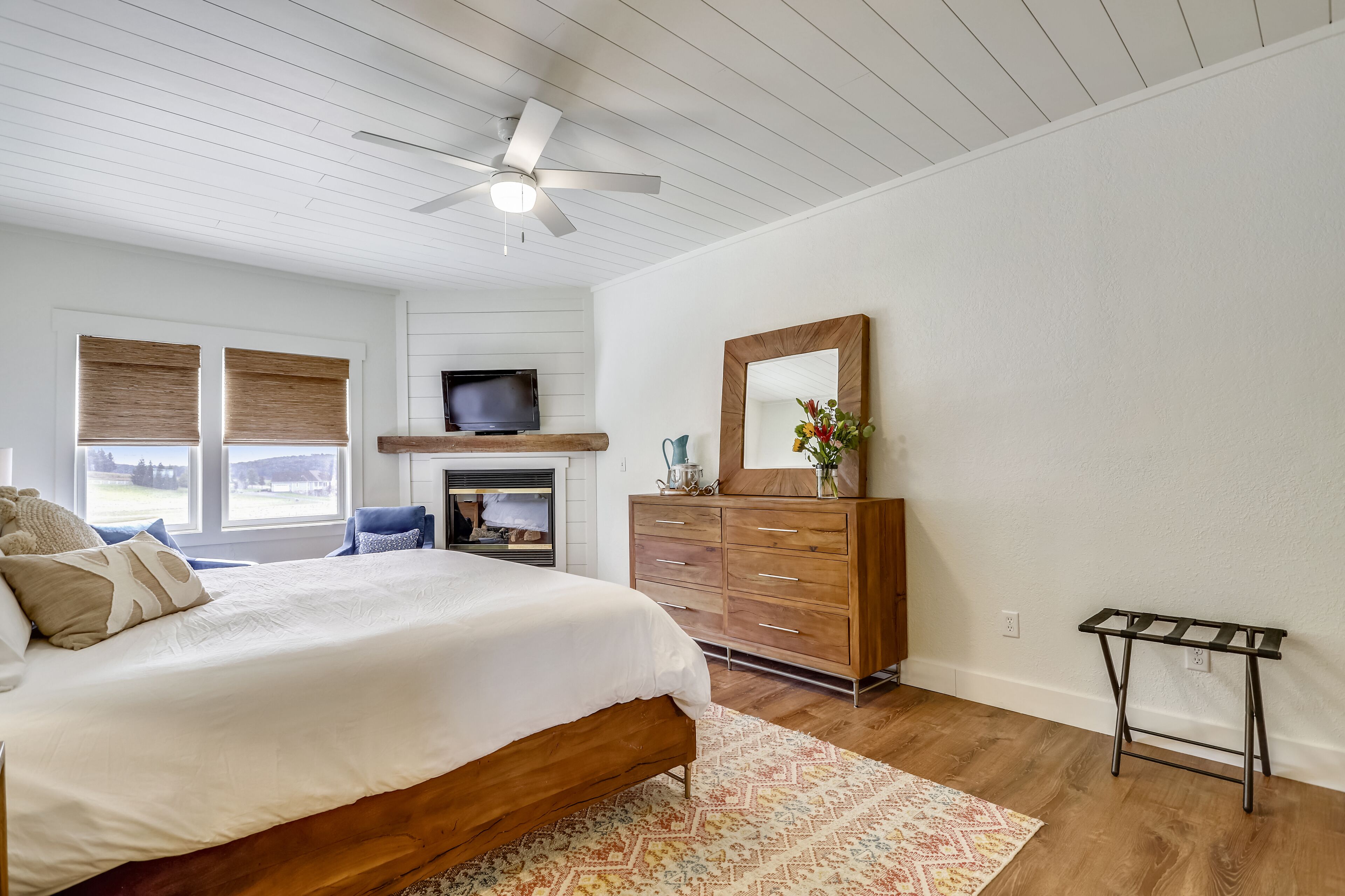 Une chambre à coucher avec un lit en bois, un ventilateur de plafond, une télévision, une commode et une petite table.