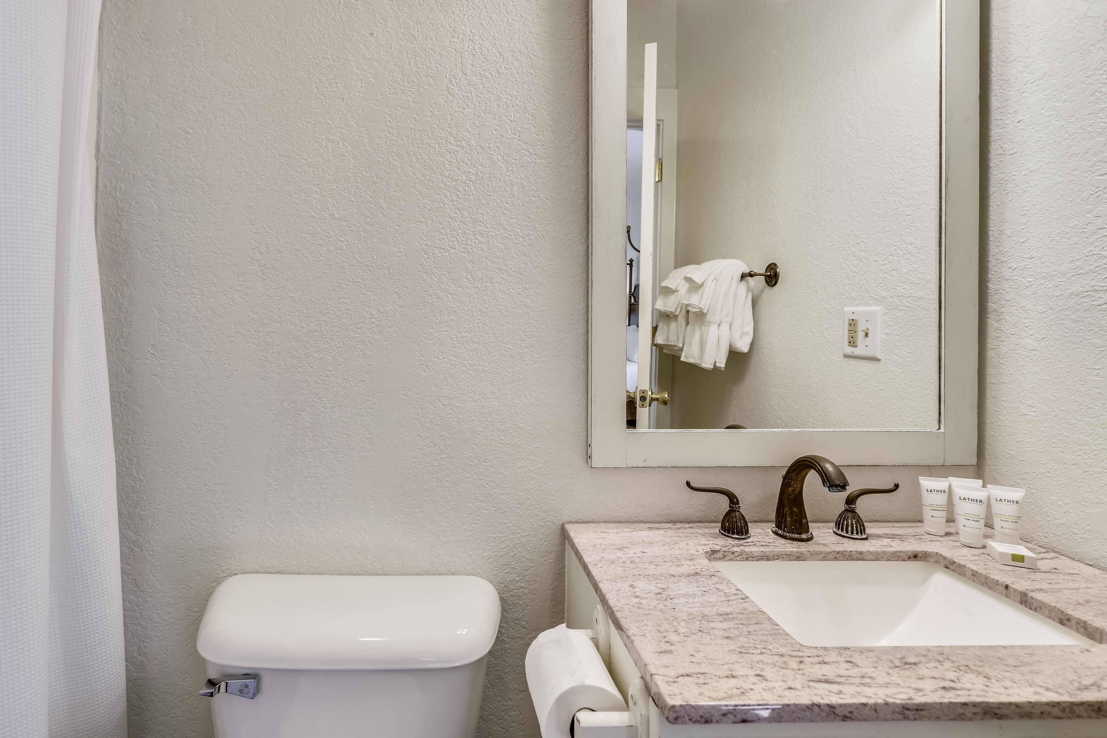Un baño con inodoro blanco, lavabo con encimera de mármol y espejo sobre el lavabo.