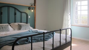 A bedroom with a bed, a headboard, a window, and a shelf with bottles. - Stylish elevated village house with stunning countryside views. (Frolois)