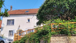 A white building with a red-tiled roof, a stone wall with greenery, and a wooden fence. - Stylish elevated village house with stunning countryside views. (Frolois)