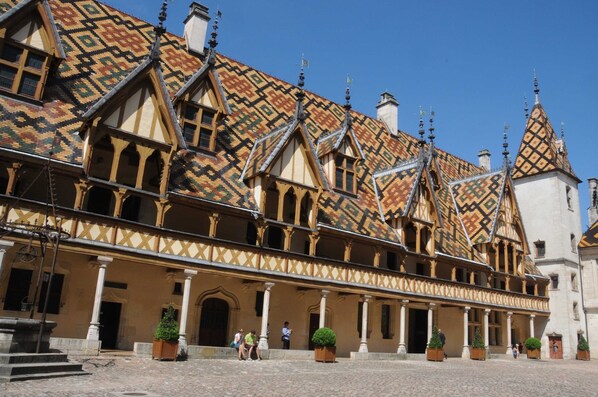 Un bâtiment historique à la façade symétrique, doté de plusieurs toits à pignons et d’une cour intérieure avec des marches menant à l’entrée.