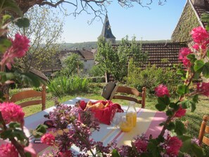 Une table dressée à l’extérieur, avec une bouteille de jus d’orange, un verre et un panier de pain.