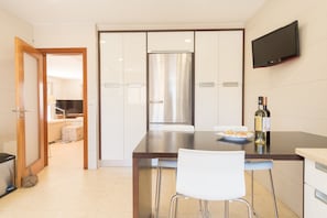 Une cuisine moderne avec un réfrigérateur en acier inoxydable, un téléviseur à écran plat fixé au mur et un coin repas comprenant une chaise blanche et une assiette de nourriture.