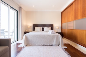 Une chambre avec un grand lit, un lambris en bois sur un des murs et une vue sur l’extérieur grâce à une grande fenêtre.
