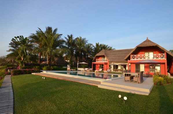 A resort with a swimming pool, lounge chairs, and a thatched-roof building.
