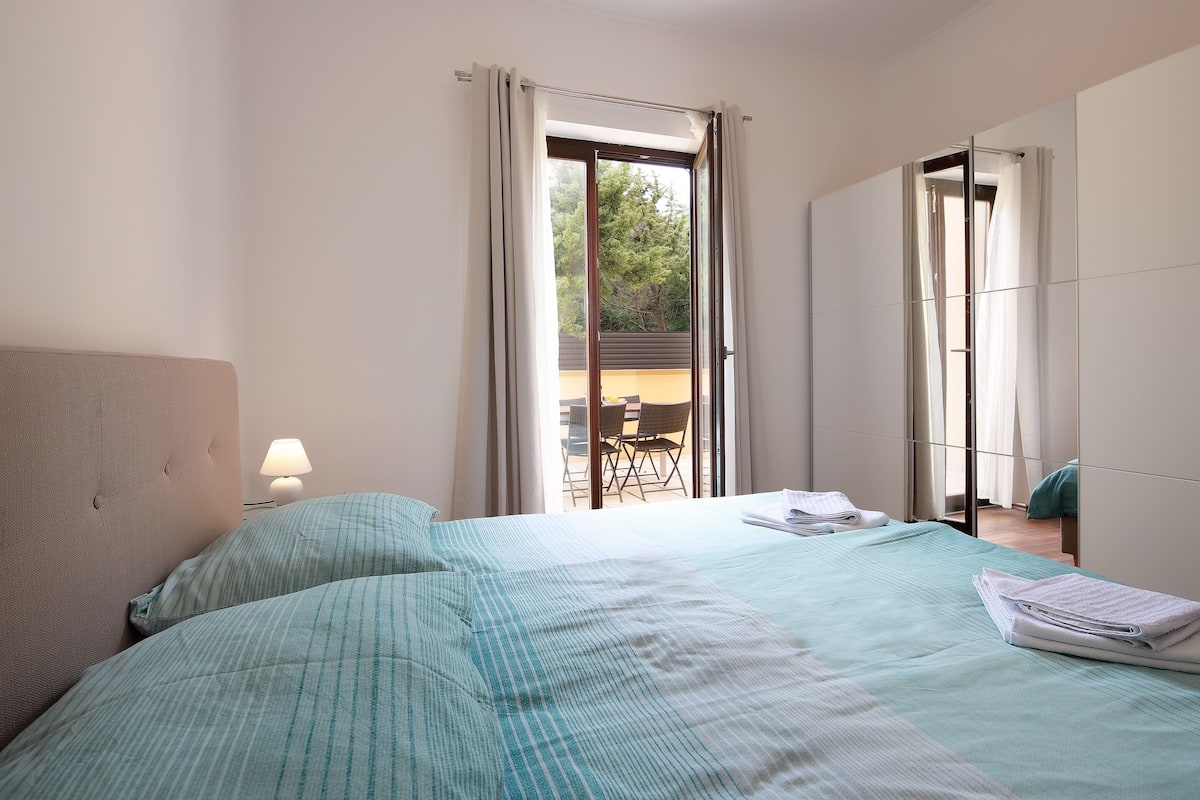 A bedroom with a bed, a nightstand, a lamp, and a view of the outside balcony.