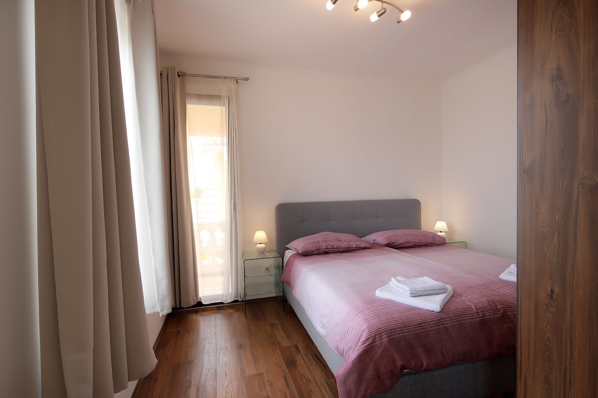 A bedroom with a bed, bedside lamps, and a window with curtains.
