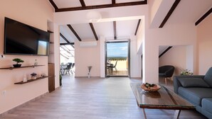 A spacious living area with a large flat-screen TV, wooden flooring, a glass coffee table, and a blue sofa. - Apartments Galboka (Mali Losinj)