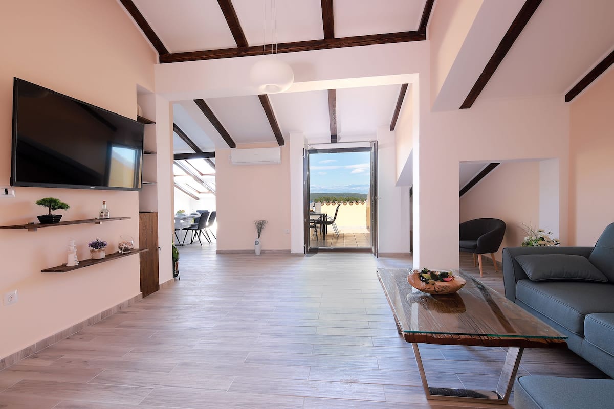 A spacious living area with a large flat-screen TV, wooden flooring, a glass coffee table, and a blue sofa.