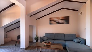 A modern living room with a glass coffee table, a grey sectional sofa, and a painting on the wall. - Apartments Galboka (Mali Losinj)