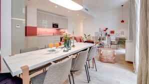 A modern kitchen with a central island, a dining area with a marble table, and a living space with a sofa and bookshelves. - Sweett | Turenne I - Three Bedroom Apartment, Sleeps 6 (Paris)