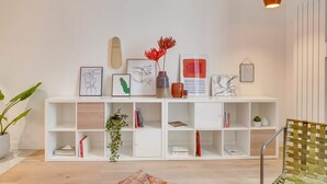 A modern living room with a white console table displaying artwork and decorative items, a green woven chair, and a wooden floor. - Sweett | Turenne I - Three Bedroom Apartment, Sleeps 6 (Paris)