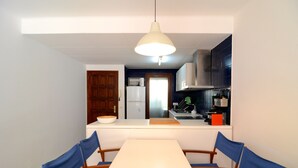 A dining area with a white table and blue chairs, a kitchen with a microwave and stove, and a hanging light fixture. - MIGJORN MAR PB (Estartit)