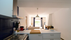 A modern kitchen with a central island, a stove, and a sink. There is a dining area with a sofa and a window with curtains. - MIGJORN MAR PB (Estartit)