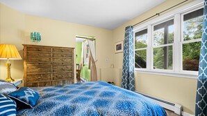 Une chambre à coucher avec un lit, une commode, une lampe et une fenêtre avec des rideaux.
