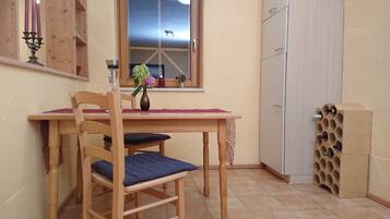 Un pequeño comedor con una mesa de madera, dos sillas, un florero con flores y una ventana con vista a un avión.