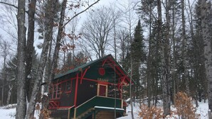 Une cabane à l’extérieur vert et aux bordures rouges, entourée de neige et d’arbres.