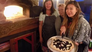 Un groupe de personnes se tient autour d’un four à pizza, et une pizza est posée sur un plat.