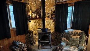 A cozy room with a stone wall, a wood-burning stove, a chair with a blanket, and a dog. - Come and enjoy some peace and quiet at the Pumpkin hollow Inn (Allegany)