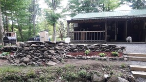 A rustic cabin with a stone wall and a wooden deck, surrounded by a forested area. - Come and enjoy some peace and quiet at the Pumpkin hollow Inn (Allegany)