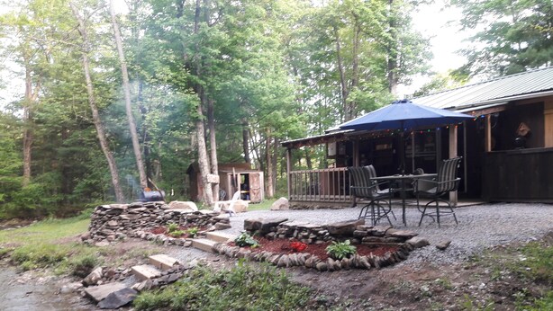 A rustic outdoor patio with stone steps leading to a seating area, surrounded by greenery and a small stream. - Come and enjoy some peace and quiet at the Pumpkin hollow Inn (Allegany)