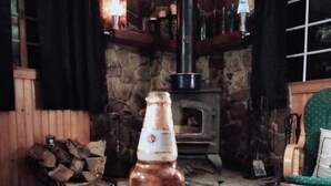A bottle of Modelo beer on a wooden table in a rustic room with a stone fireplace and wooden furniture. - Come and enjoy some peace and quiet at the Pumpkin hollow Inn (Allegany)