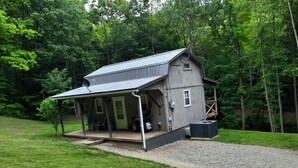 Une petite cabane rustique dotée d’un porche, d’un espace extérieur couvert aménagé en coin salon et d’une grande fenêtre.