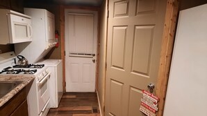 Une petite cuisine équipée d’une cuisinière, d’un four à micro-ondes et d’une porte blanche sur laquelle est apposée une pancarte.
