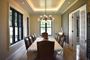 Une salle à manger avec une longue table, des chaises, un lustre et de grandes fenêtres.