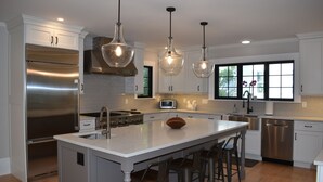 Una cocina moderna con una isla central, electrodomésticos de acero inoxidable, iluminación colgante y un amplio ventanal.