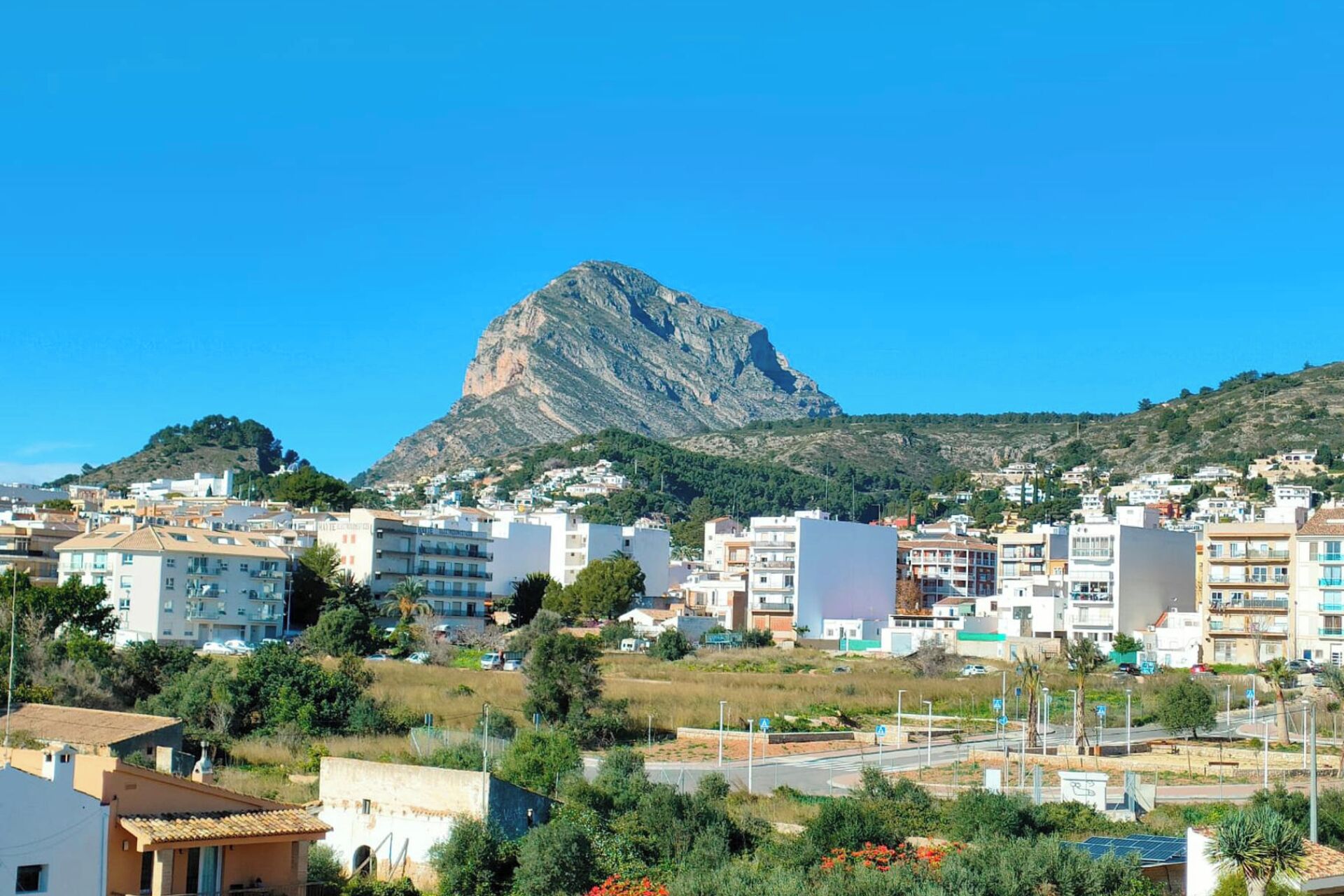 Eine Küstenstadt mit modernen Gebäuden, ein markanter Berg im Hintergrund und ein klarer, blauer Himmel.